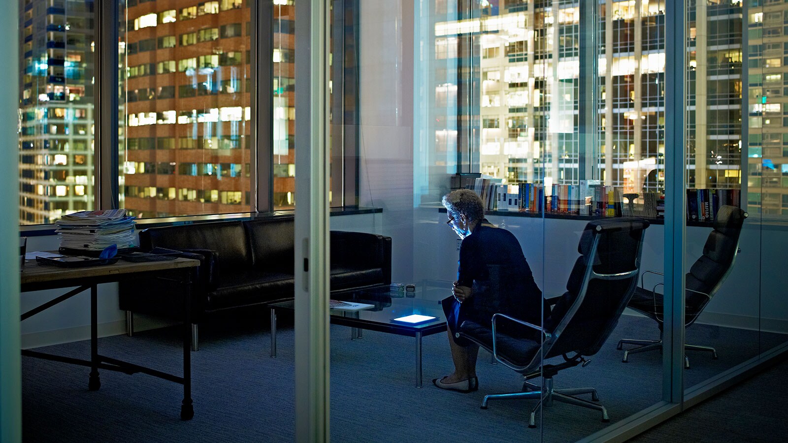 Woman sitting in the office ar night with a view of buildings with lights on