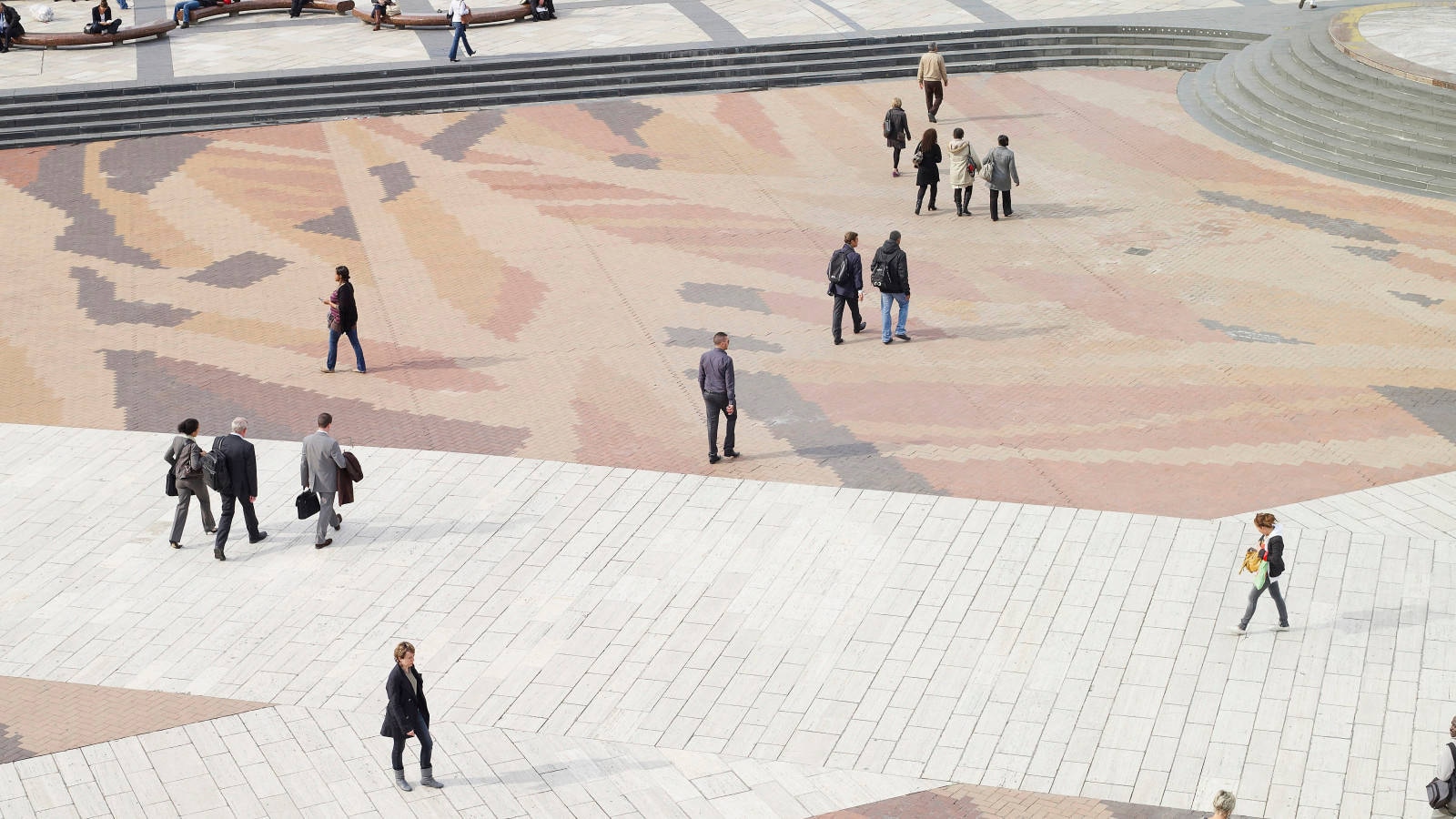 scarrered pedestrains walking outside a public space with a patterned surface 